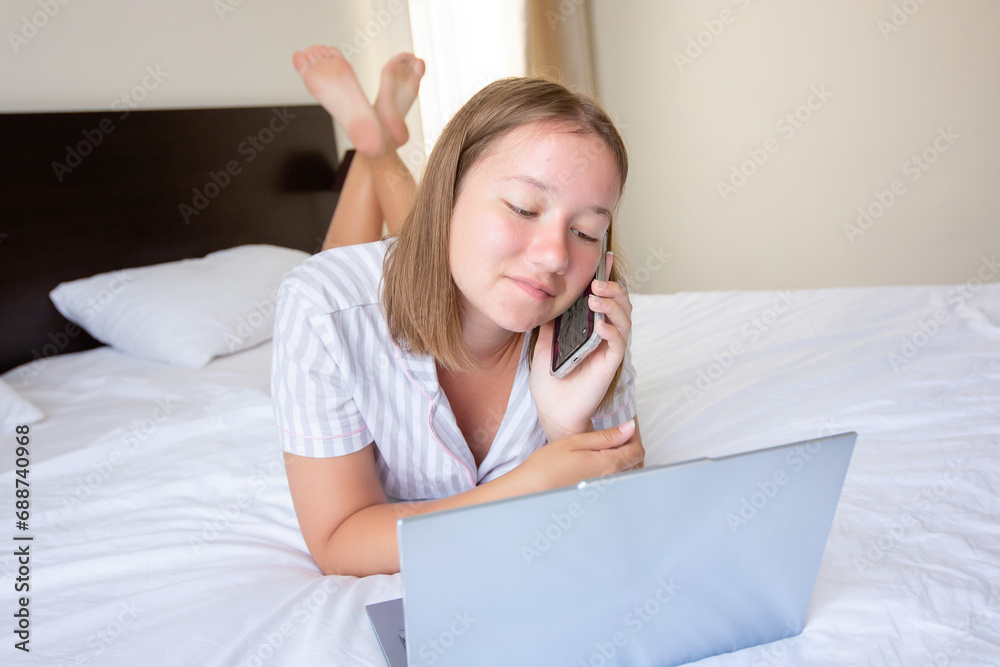 Happy confident young woman with a friendly smile lying relaxing in bed with her laptop computer Happy confident young woman with a friendly smile lying relaxing in bed with her laptop computer