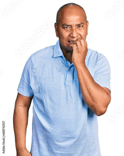 Hispanic middle age man wearing casual t shirt looking stressed and nervous with hands on mouth biting nails. anxiety problem.
