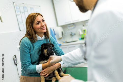 Fototapeta Naklejka Na Ścianę i Meble -  Young man, a veterinarian by profession, examines a dog in modern vet clinic.Young owner helps to calm down the pet and talks with the vet specialist.