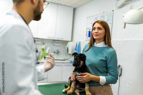 Fototapeta Naklejka Na Ścianę i Meble -  Young man, a veterinarian by profession, examines a dog in modern vet clinic.Young owner helps to calm down the pet and talks with the vet specialist.