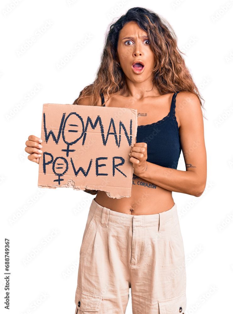 Young hispanic woman with tattoo holding woman power banner scared and amazed with open mouth for surprise, disbelief face Young hispanic woman with tattoo holding woman power banner scared and amazed with open mouth for surprise, disbelief face