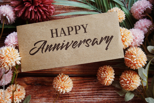 Happy Anniversary text message with flower decoration on wooden background