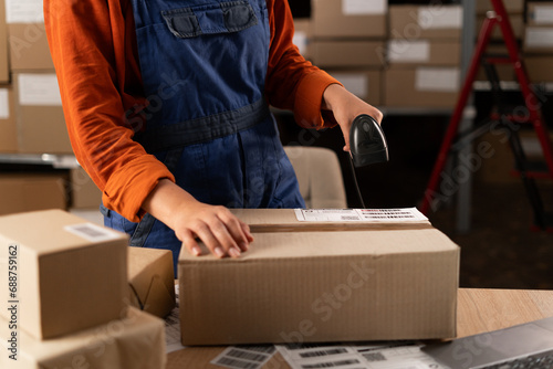 Close-up of female hands scanning barcode on delivery parcel box with scanner. Worker scan barcode before delivery at storage.