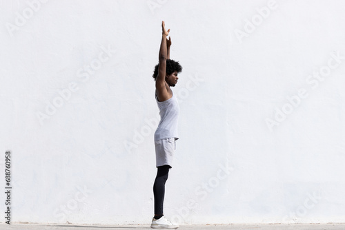 Full body side view of confident African American male athlete in activewear with concentration stretching arms while standing looking away against white background photo