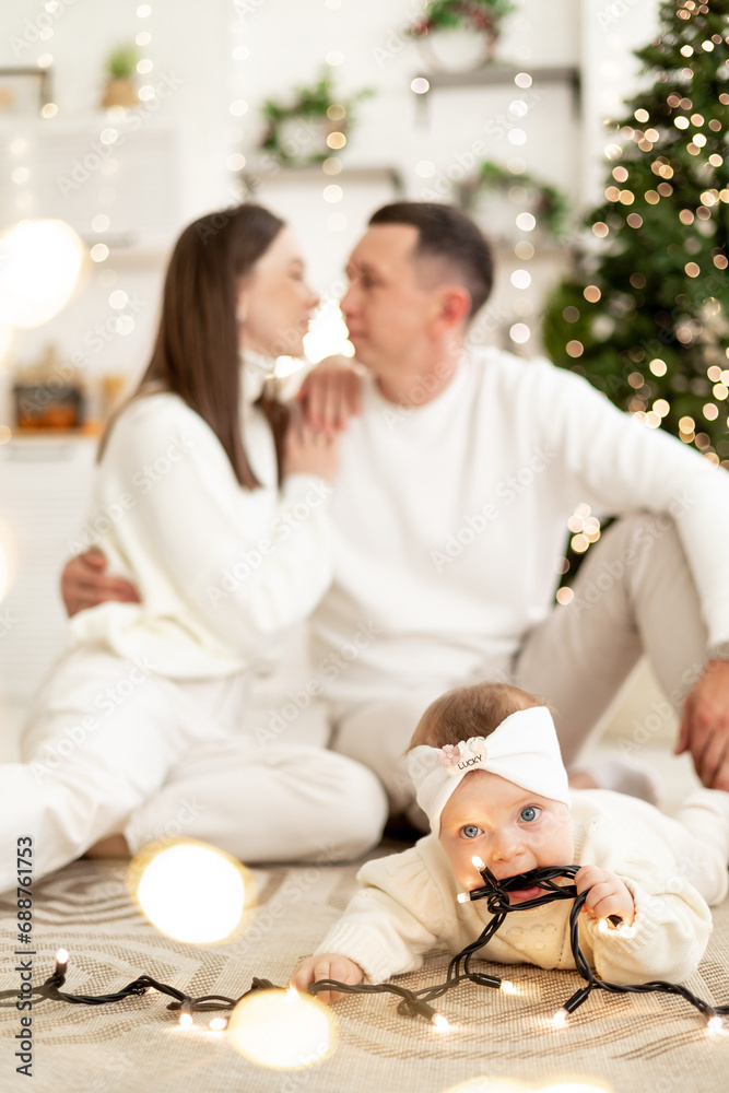 a small child with a garland in focus against the background of kissing happy parents, smiling, kissing and hugging congratulating each other celebrates the New Year holiday a small child with a garland in focus against the background of kissing happy parents, smiling, kissing and hugging congratulating each other celebrates the New Year holiday