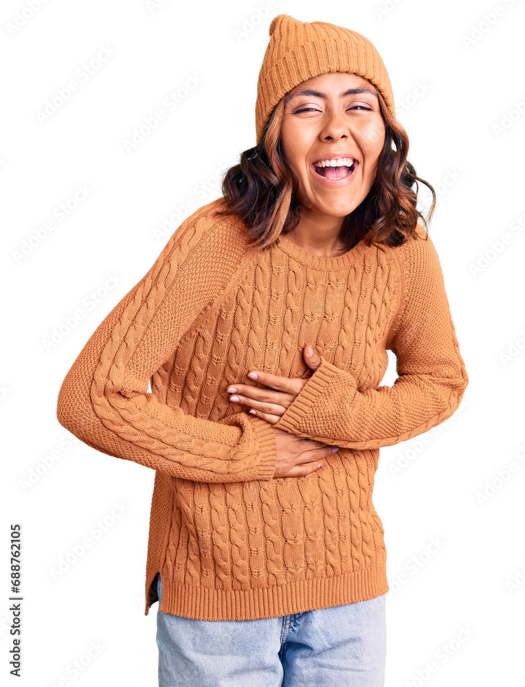 Young beautiful mixed race woman wearing wool sweater and winter hat smiling and laughing hard out loud because funny crazy joke with hands on body. Young beautiful mixed race woman wearing wool sweater and winter hat smiling and laughing hard out loud because funny crazy joke with hands on body.