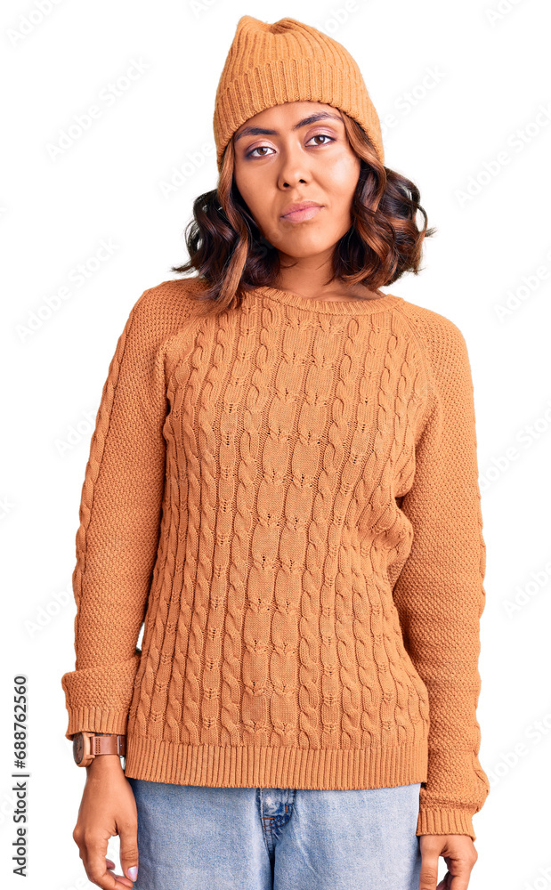 Young beautiful mixed race woman wearing wool sweater and winter hat relaxed with serious expression on face. simple and natural looking at the camera. Young beautiful mixed race woman wearing wool sweater and winter hat relaxed with serious expression on face. simple and natural looking at the camera.