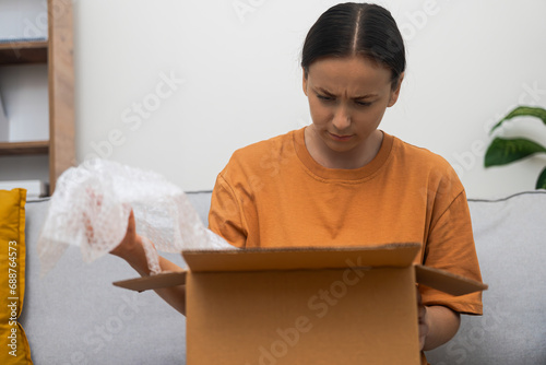 Haywire female client inspects box of goods holding filler for transportation safety woman upset by inappropriate item delivered to home sitting on sofa photo