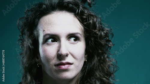 Disinterested expression of woman rolling eyes discrediting expressed views, tight close-up face of female person in 20s behind teal background