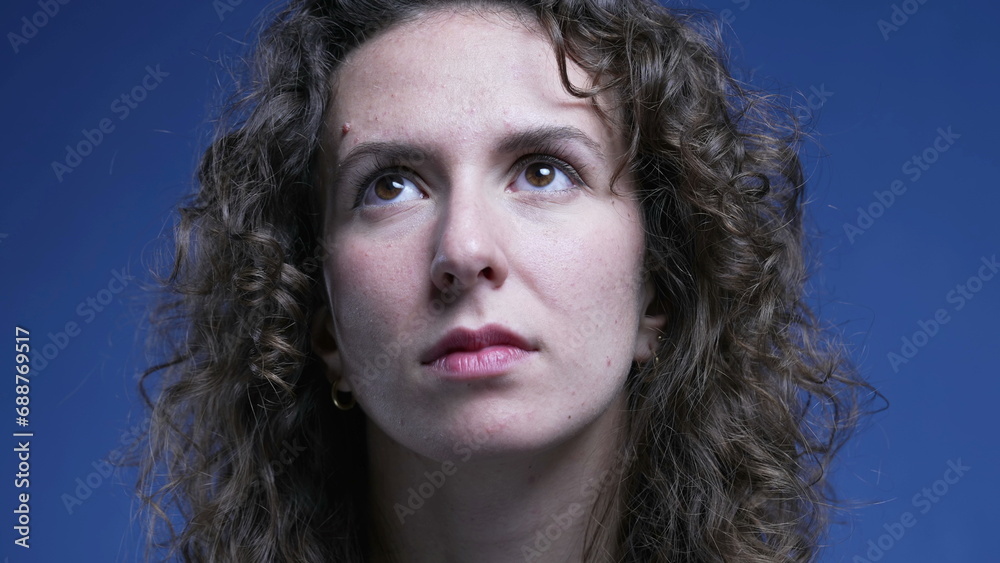 Portrait of a happy young woman smiling at camera on blue backdrop. Female 20s person with curly hairPortrait of a happy young woman smiling at camera on blue backdrop. 