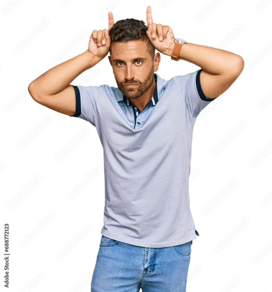 Handsome man with beard wearing casual clothes doing funny gesture with finger over head as bull horns Handsome man with beard wearing casual clothes doing funny gesture with finger over head as bull horns
