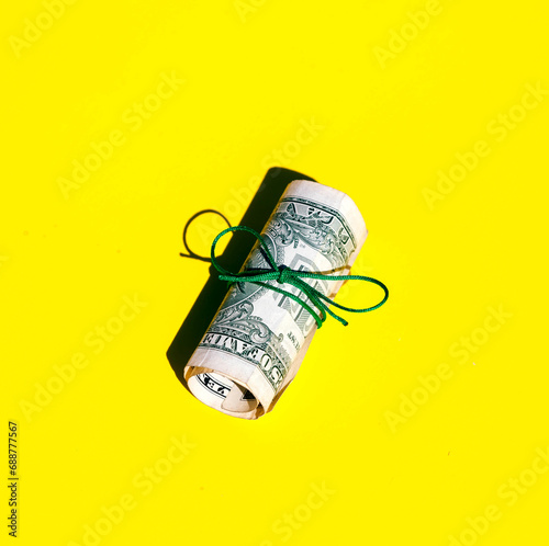 Closeup of rolled one dollar paper currency tied on yellow background with copy space photo