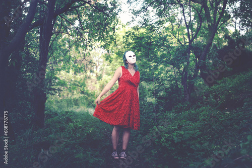 woman with mask on her face and red dress dancing in a forest, abstract concept