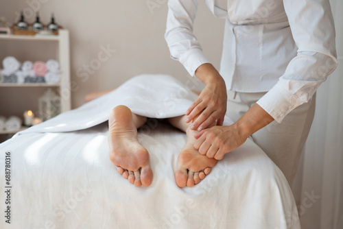 Crop hands of anonymous female therapist massaging foot of customer lying on bed to relieve pain by gently pressing pressure points at spa salon photo