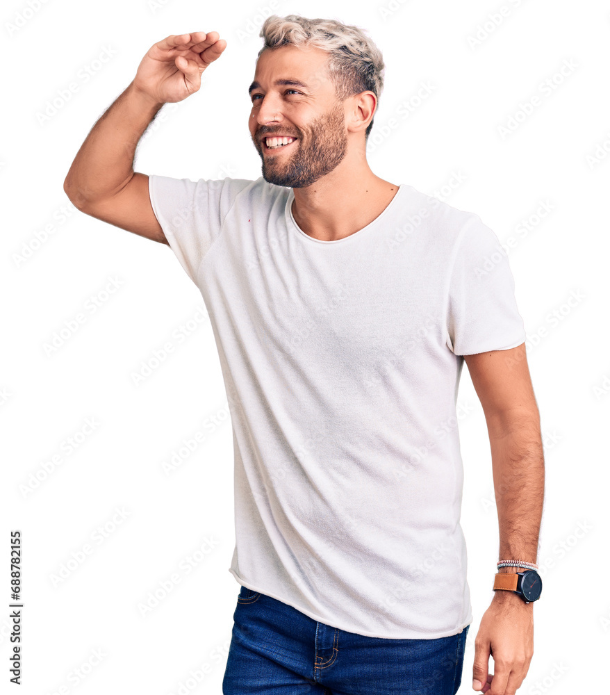 Young handsome blond man wearing casual t-shirt very happy and smiling looking far away with hand over head. searching concept. Young handsome blond man wearing casual t-shirt very happy and smiling looking far away with hand over head. searching concept.