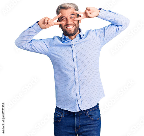 Young handsome blond man wearing elegant shirt doing peace symbol with fingers over face, smiling cheerful showing victory