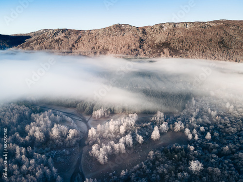 Clouds over the mountains and forest at foggy sunrise. Aerial view.