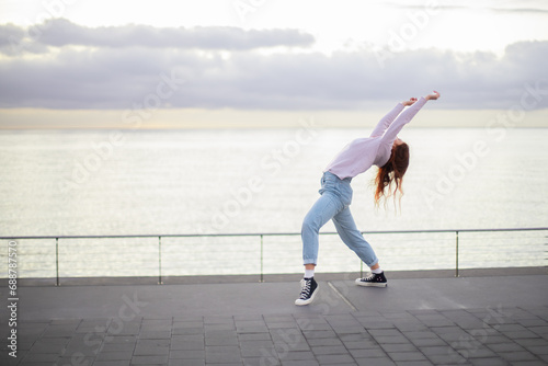 Young beautiful woman dancing contemporary style in front of the sea at sunrise.