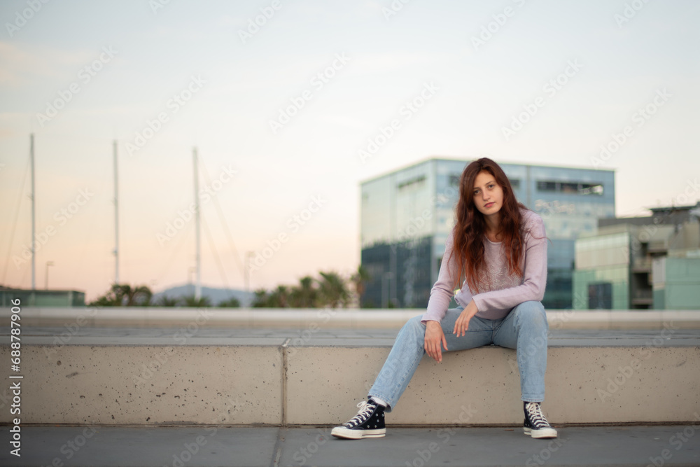 Fototapeta premium Young woman in casual clothes posing in front of an urban setting at sunrise.