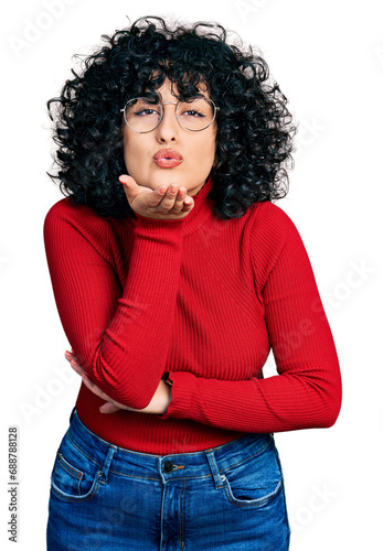 Young middle east girl wearing casual clothes and glasses looking at the camera blowing a kiss with hand on air being lovely and sexy. love expression.