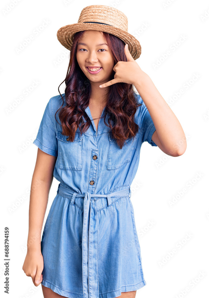 Young beautiful chinese girl wearing summer hat smiling doing phone gesture with hand and fingers like talking on the telephone. communicating concepts. Young beautiful chinese girl wearing summer hat smiling doing phone gesture with hand and fingers like talking on the telephone. communicating concepts.