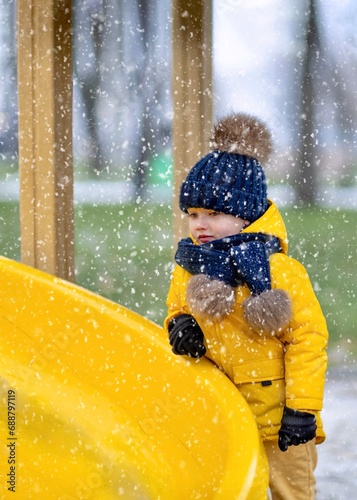 Fototapeta Naklejka Na Ścianę i Meble -  A joyful toddler playing on a playground in a park in winter.