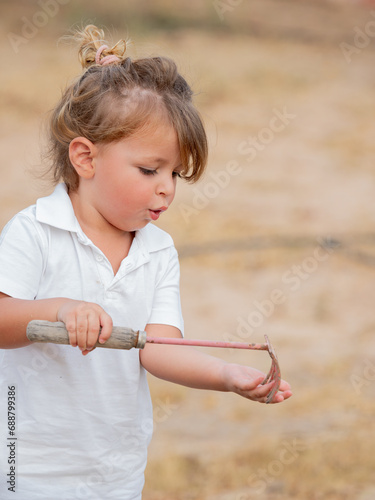 Side view of little boy holding hand rake while standing in backyard photo