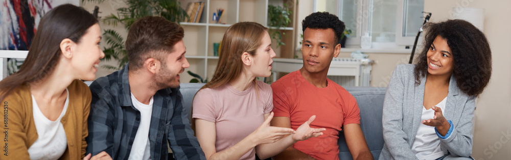 Spending time with friends. Group of young multicultural people in casual wear talking and resting together while sitting on the sofa at home. They enjoying time together Spending time with friends. Group of young multicultural people in casual wear talking and resting together while sitting on the sofa at home. They enjoying time together