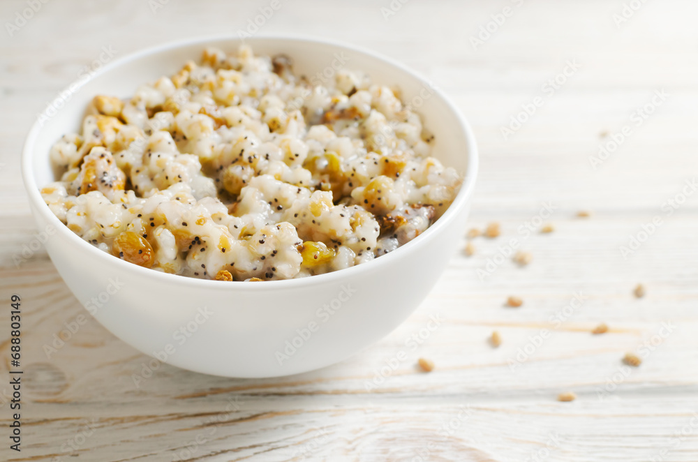 Kutya, a traditional Ukrainian Christmas dish made of wheat groats on the table for Christmas or the old New Year. Boiled porridge with walnuts, raisins, poppy seeds and honey in a white bowl. Kutya, a traditional Ukrainian Christmas dish made of wheat groats on the table for Christmas or the old New Year. Boiled porridge with walnuts, raisins, poppy seeds and honey in a white bowl.