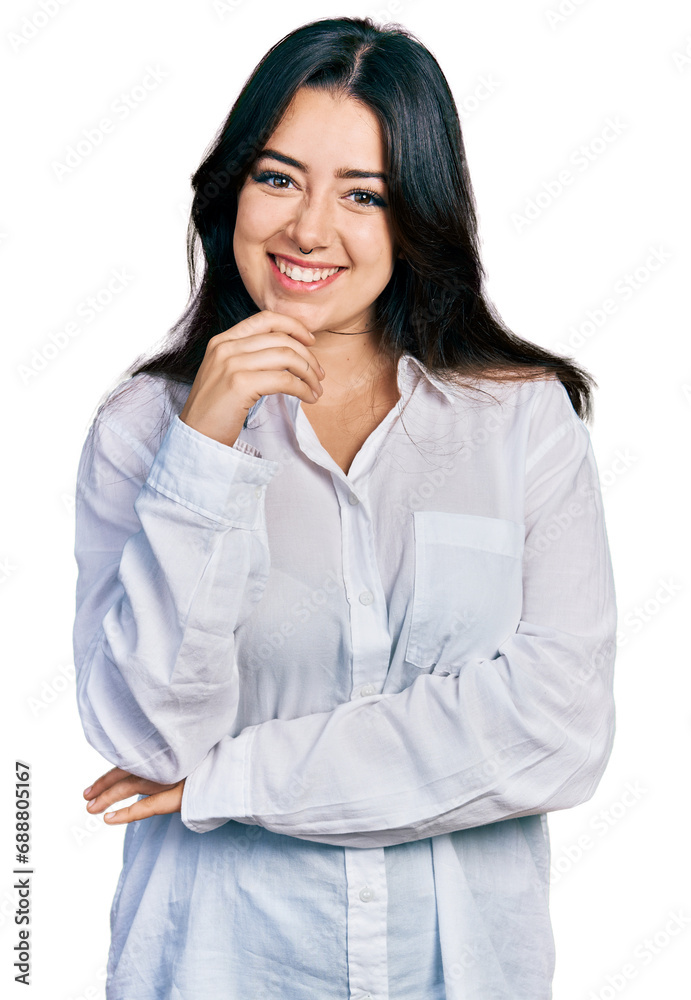 Beautiful hispanic woman wearing casual white shirt looking confident at the camera with smile with crossed arms and hand raised on chin. thinking positive. Beautiful hispanic woman wearing casual white shirt looking confident at the camera with smile with crossed arms and hand raised on chin. thinking positive.