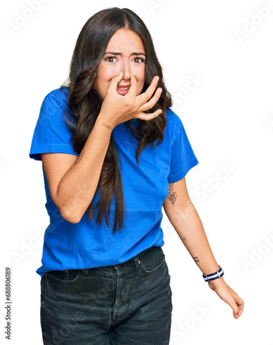 Beautiful brunette young woman wearing casual clothes smelling something stinky and disgusting, intolerable smell, holding breath with fingers on nose. bad smell