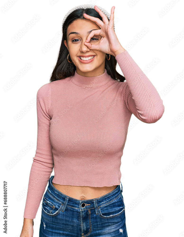Young hispanic girl wearing casual clothes doing ok gesture with hand smiling, eye looking through fingers with happy face. Young hispanic girl wearing casual clothes doing ok gesture with hand smiling, eye looking through fingers with happy face.