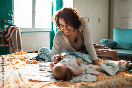 Smiling young happy mother playing in bed with her baby photo