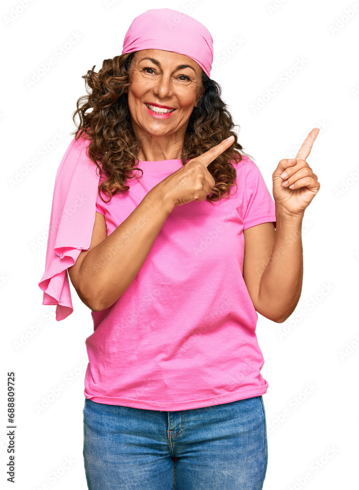 Middle age hispanic woman wearing breast cancer support pink scarf smiling and looking at the camera pointing with two hands and fingers to the side. Middle age hispanic woman wearing breast cancer support pink scarf smiling and looking at the camera pointing with two hands and fingers to the side.