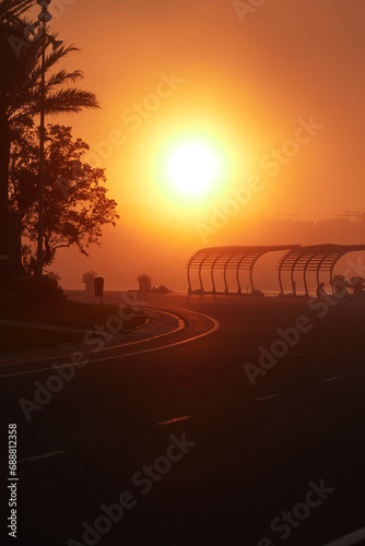 Magnificent sunset during heavy fog. Empty road and silhouettes of trees and recreation areas with sun protection along the marina pier © Anna Baranova
