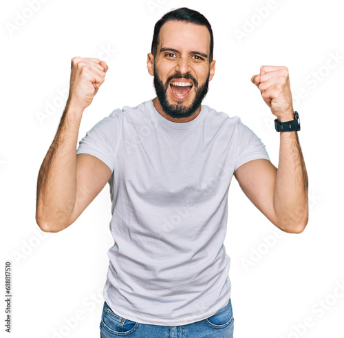 Young man with beard wearing casual white t shirt angry and mad raising fists frustrated and furious while shouting with anger. rage and aggressive concept.