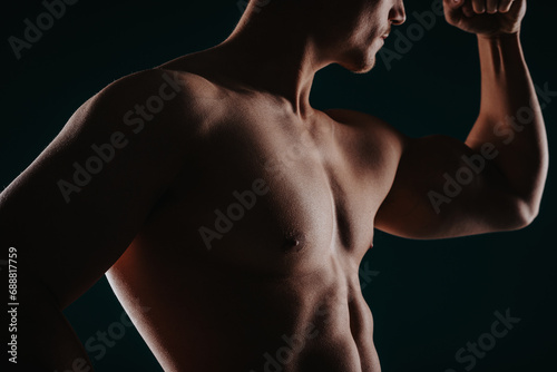 Muscular and good-looking man standing in a dark room and flexing his bicep