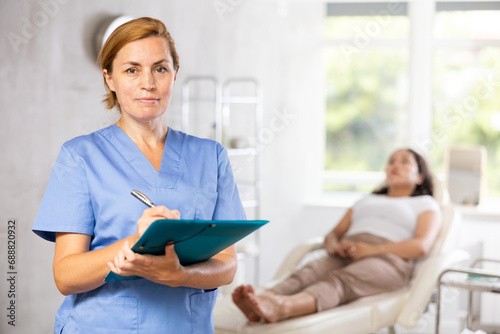 Portrait shot of female doctor holding clipboard in hand while standing in medical esthetic office