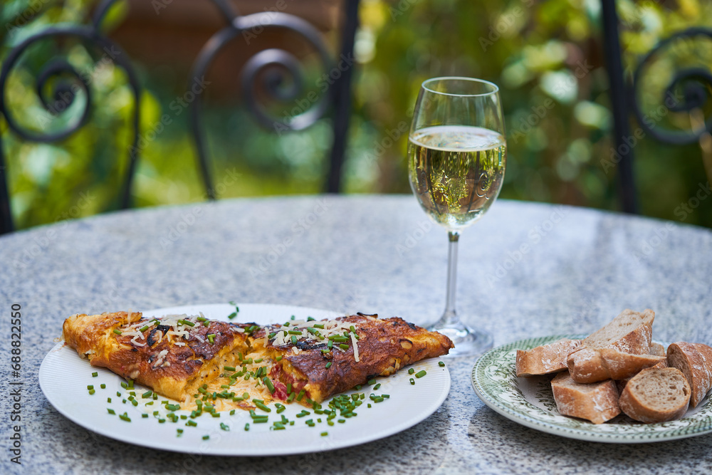 Delicious egg omelette with sheep cheese served on white porcelain plate as a light quick lunch with slices of whole grain baguette and glass of white wine outside in the garden restaurant or bistro.