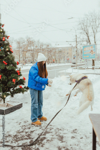 A beautiful young girl throws snow and plays with her white dog in winter, Festive New Year's mood, happy woman with a dog