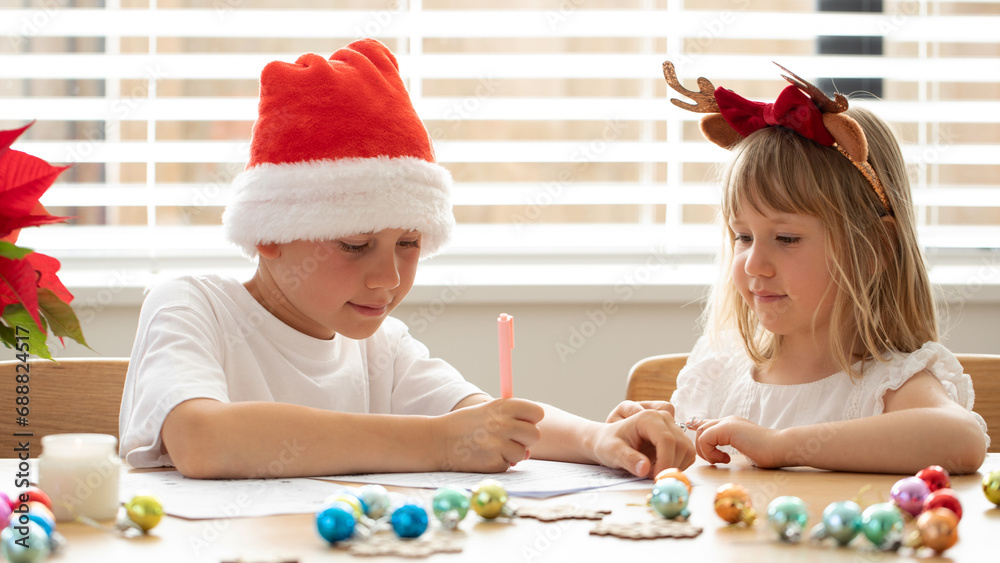 Naklejka premium Cute brother and sister in Christmas costumes are writing a letter to Santa Claus. New Year's Eve 