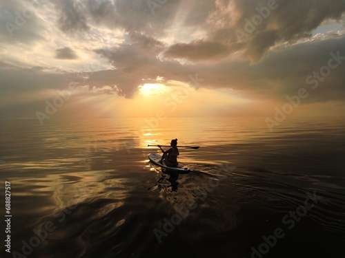 silhouette of a girl on a boat with an oar on the sea  in a calm  with a small surf  against the backdrop of dark clouds in the evening  before sunset