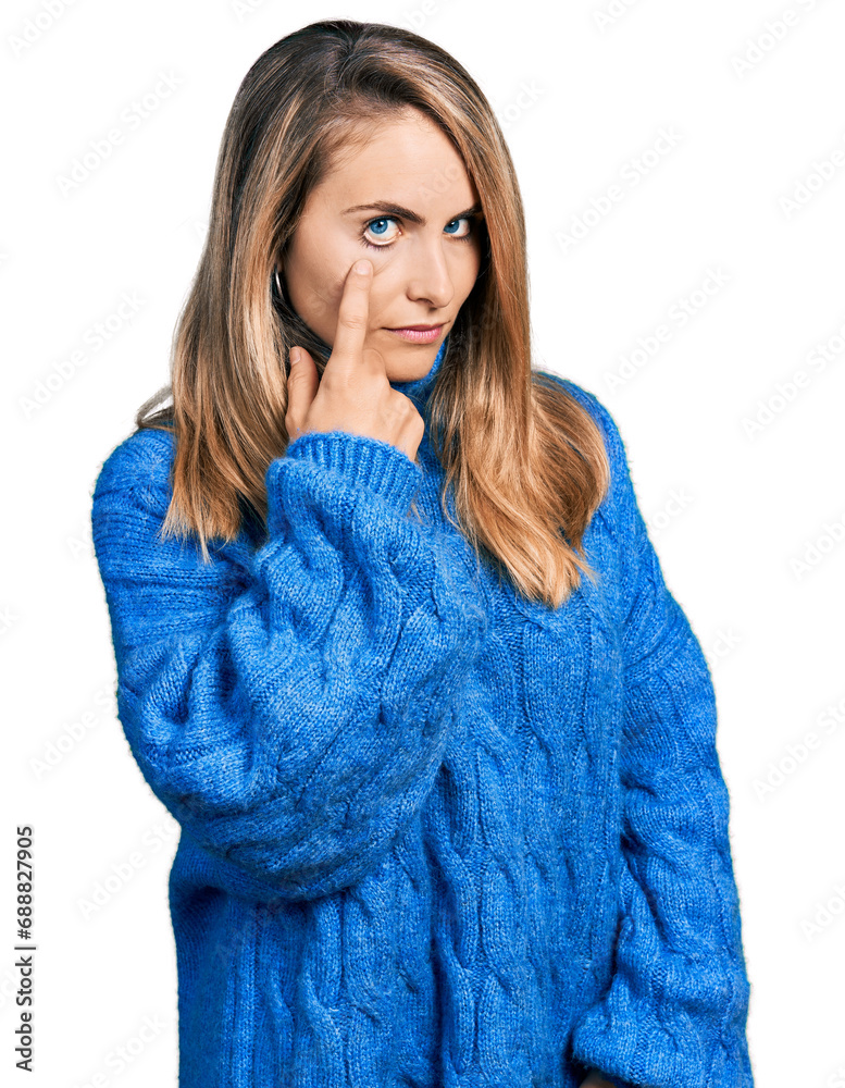 Young blonde woman wearing casual sweater pointing to the eye watching you gesture, suspicious expression