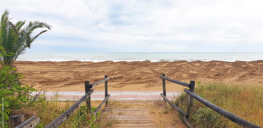 Wooden path through the sandy shore to the sea. Panorama.