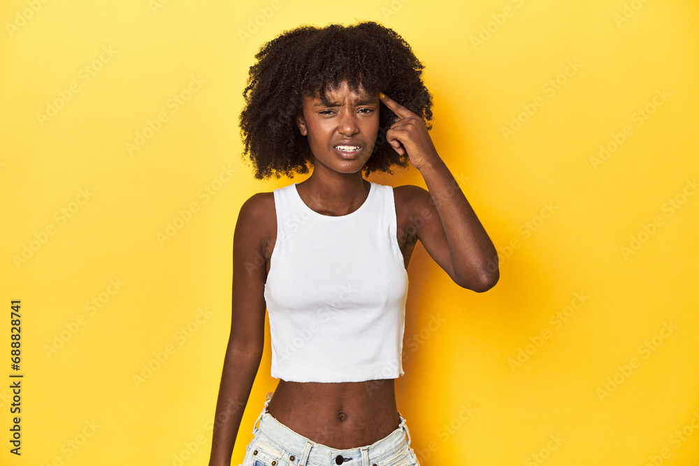 Teen girl in white tank top, yellow studio background showing a disappointment gesture with forefinger. Teen girl in white tank top, yellow studio background showing a disappointment gesture with forefinger.