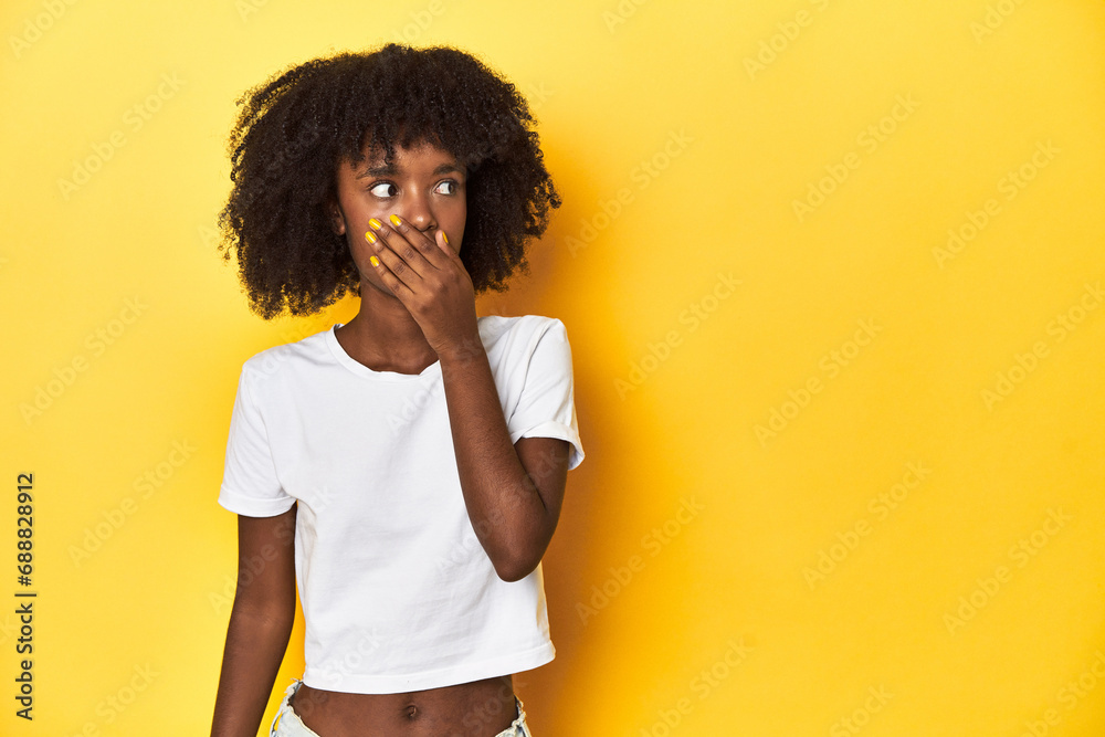Teen girl in classic white T-shirt, yellow studio backdrop thoughtful looking to a copy space covering mouth with hand. Teen girl in classic white T-shirt, yellow studio backdrop thoughtful looking to a copy space covering mouth with hand.
