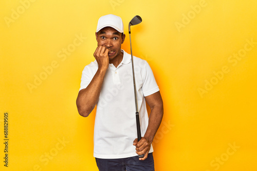 African American man golfer  yellow studio backdrop  biting fingernails  nervous and very anxious.