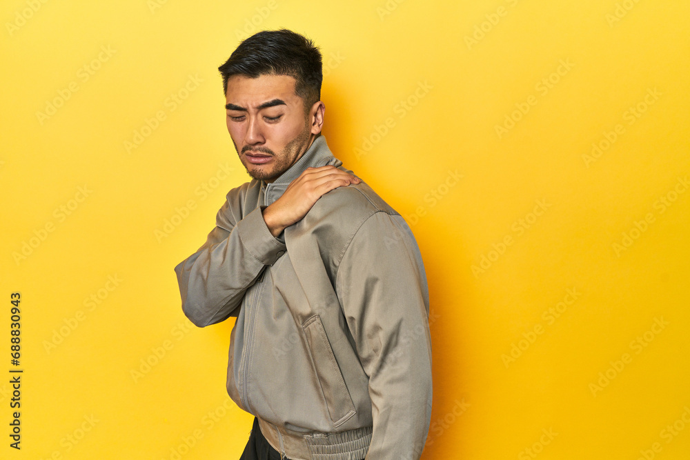 Stylish Asian man in gray jacket on yellow studio having a shoulder pain. Stylish Asian man in gray jacket on yellow studio having a shoulder pain.