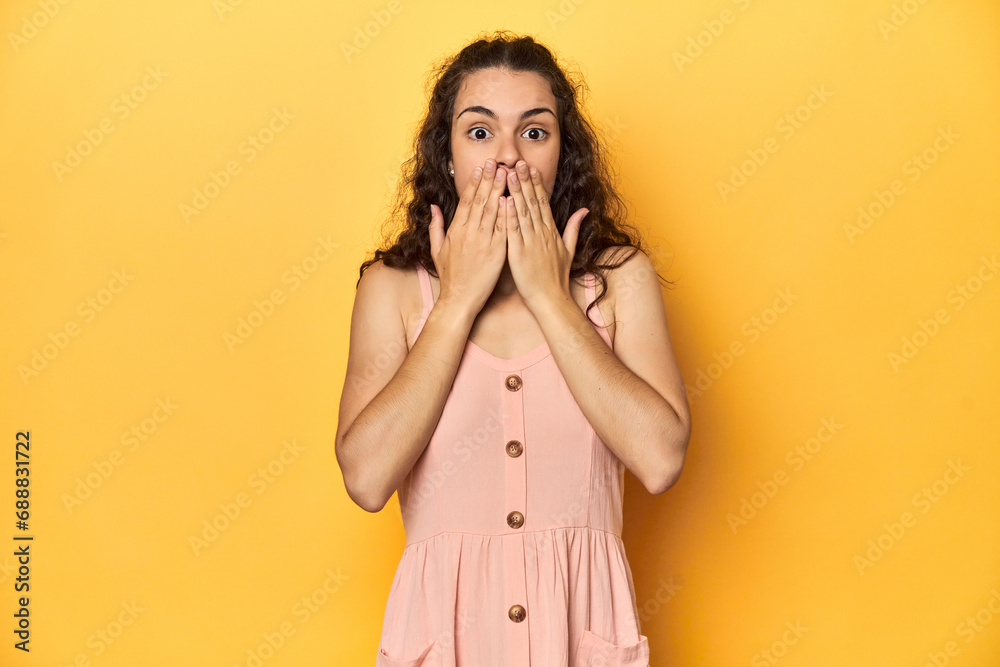 Young Caucasian woman, yellow studio background, shocked, covering mouth with hands, anxious to discover something new. Young Caucasian woman, yellow studio background, shocked, covering mouth with hands, anxious to discover something new.