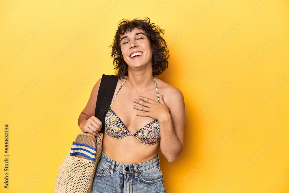 Caucasian woman in bikini with beach bag, studio laughs out loudly keeping hand on chest. Caucasian woman in bikini with beach bag, studio laughs out loudly keeping hand on chest.